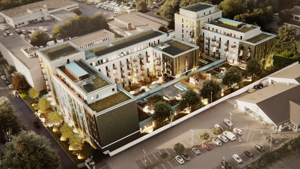 Luftaufnahme der Vogelsanger Höfe, eines modernen, mehrstöckigen Wohn- und Geschäftshauskomplexes mit begrünten Dächern, Balkonen, einem zentralen Innenhof und umliegenden Parkplätzen.
